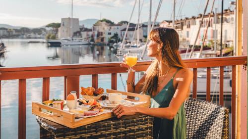a woman sitting on a balcony with a tray of food at Le Suffren Hôtel in Grimaud