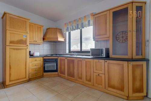 a large kitchen with wooden cabinets and a window at Cosy 2BR penthouse with private balcony by 360 Estates in Siġġiewi