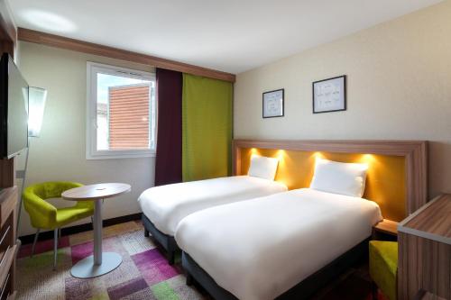a hotel room with two beds and a chair at Mercure Libourne Saint Emilion in Libourne