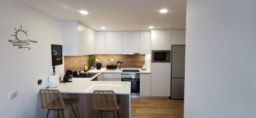 a kitchen with white cabinets and a kitchen island with chairs at Apartamento Varanda do Sol in Monte Gordo