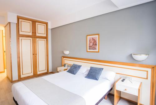 a bedroom with a white bed with two blue pillows at Hotel Alda Boiro in Boiro
