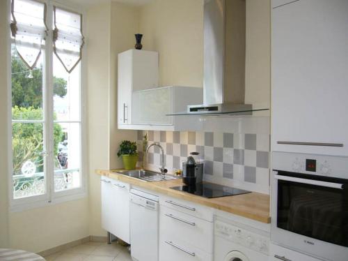 une cuisine avec des armoires blanches, un évier et une fenêtre dans l'établissement Centre Ville Calme Festivales Plages, à Cannes