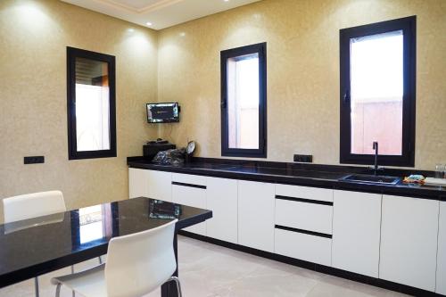 a kitchen with white cabinets and a table and two windows at VILLA NOÛR PALACE avec piscine jaccuzi à Marrakech in Marrakech