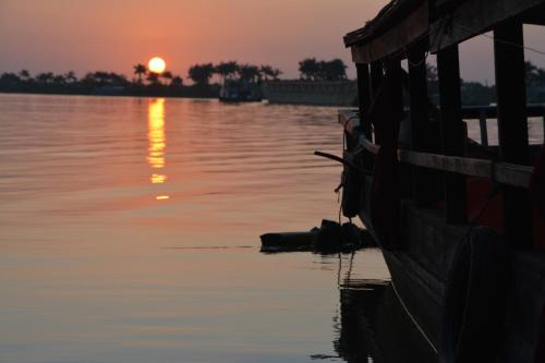 a boat in the water with a sunset in the background at Happy Family Guesthouse in Vĩnh Long