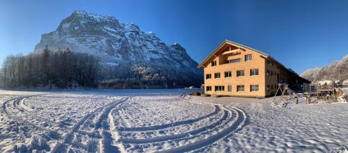 a snow covered field with a building and a mountain at Ferienwohnung Berchtold in Schnepfau