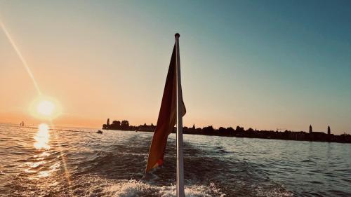 a boat with a flag in the water at sunset at Ferienwohnung Luxus & Lifestyle - Luxuriös, exklusiv, traumhaft schön mit Aufzug in Lindau