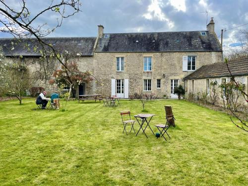 a large stone house with chairs and a table in the yard at Les chambres d'Omaha Beach Etablissement avec deux chambres d'hôtes, petit-déjeuner compris fait-maison et produits locaux in Vierville-sur-Mer