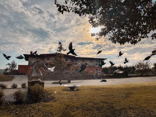 a flock of birds flying around a statue in front of a building at Hotel Rappenhof in Breuna