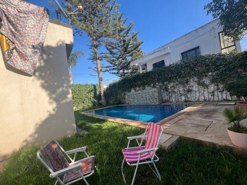 two chairs sitting in the grass next to a swimming pool at Villa Lalla Laroussa in Kenitra