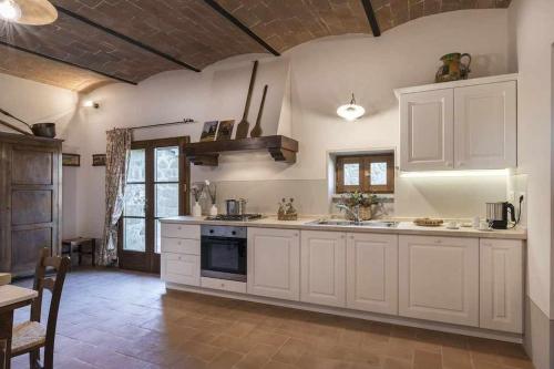 a large kitchen with white cabinets and a table at Villa I Cipressini piscina riscaldata spa Toscana in Pienza