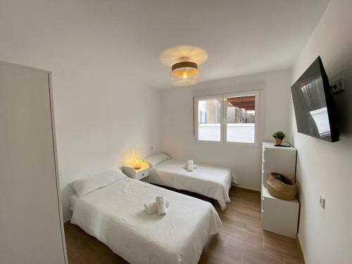 a white room with two beds and a television at Apartamento Trascuesta, PLENO CENTRO in Sanlúcar de Barrameda