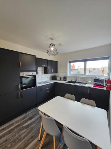 a kitchen with black cabinets and a white table and chairs at Market Quarter Apartment, town centre, free parking and wifi in Southport
