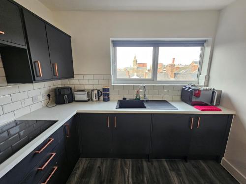 a kitchen with black cabinets and a sink and a window at Market Quarter Apartment, town centre, free parking and wifi in Southport