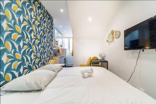 Cette chambre comprend un grand lit blanc et une télévision murale. dans l'établissement Magenta, Charmant & Moderne, à Villeurbanne