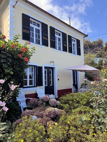 a white house with black shutters and two chairs in a garden at Quinta das Hortênsias in Arco de São Jorge
