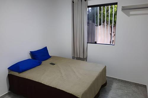a bedroom with a bed with blue pillows and a window at Casa de Temporada Guriri com Piscina - Cod 17 in São Mateus