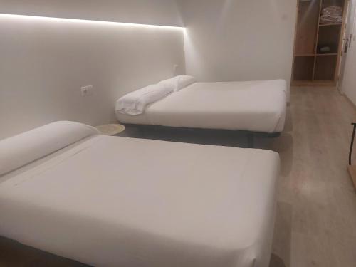 two beds in a small room with white sheets at U-Hotel Darío Lugo in Lugo