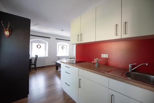 a kitchen with white cabinets and a red wall at Königswirt Historischer Landgasthof in Marktoberdorf