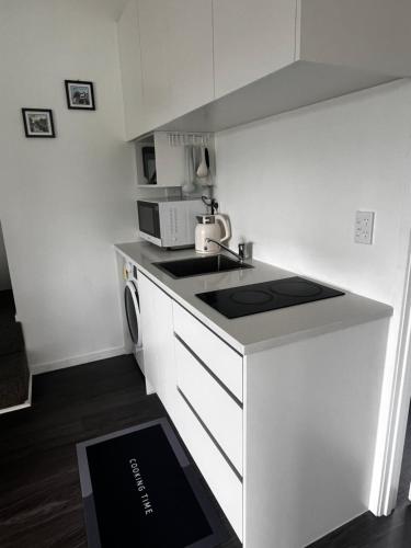 a white kitchen with a sink and a microwave at U&U 2bedrooms Home in Whangaparaoa