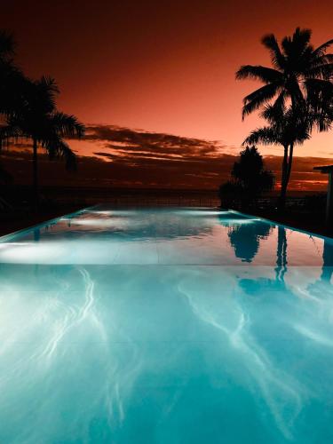 a large swimming pool with palm trees and a sunset at Villa TE URA Beach in Paea