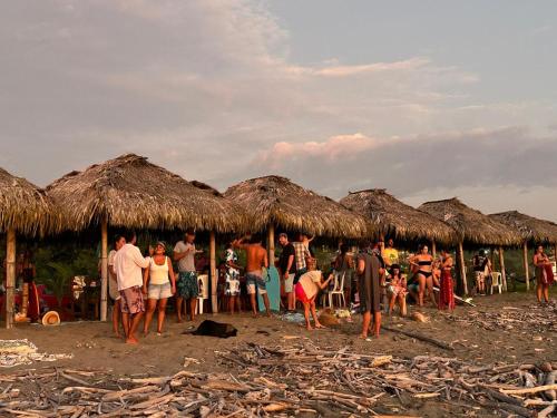 a group of people standing under huts on the beach at Wipeout Cabaña Restaurant in Las Tunas