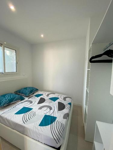 Cette chambre blanche dispose d'un lit avec des oreillers bleus. dans l'établissement La Maisonnette T2 charmant jardin parking La Cadière d'Azur 1 à 4 personnes, à La Cadière-dʼAzur