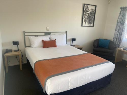 a bedroom with a large bed and a chair at Camelot Motor Lodge and Conference Centre in Palmerston North