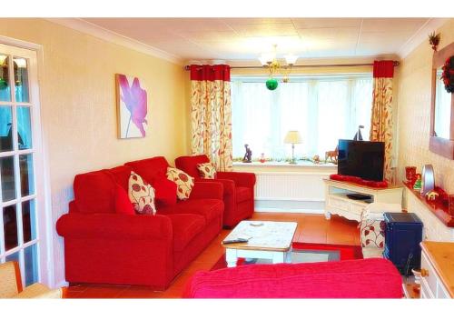 ein Wohnzimmer mit einem roten Sofa und einem Fernseher in der Unterkunft Amazing Family Cottage Just mins to Beach & Attractions, 3 bed, Sleeps 5, Large Garden, Off Road Private Parking, Fab Free WiFi & Pets are Welcome too! in Chapel Saint Leonards