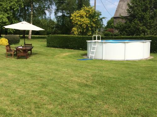 a pool with a table and an umbrella in a yard at La Crepelliere in Villedieu-les-Poëles