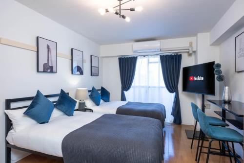 two beds in a hotel room with a tv on the wall at Nakatsu Sakae Manshon in Osaka