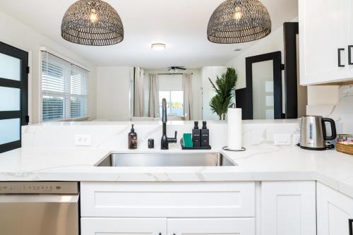 a white kitchen with a sink and two pendant lights at Newly Built Coastal Home with Yard in San Diego
