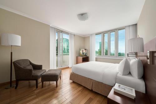 a bedroom with a bed and a chair and windows at Somerset Chancellor Court Ho Chi Minh City in Ho Chi Minh City