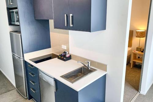 a small kitchen with blue cabinets and a sink at Ramada Suites by Wyndham Albany in Auckland