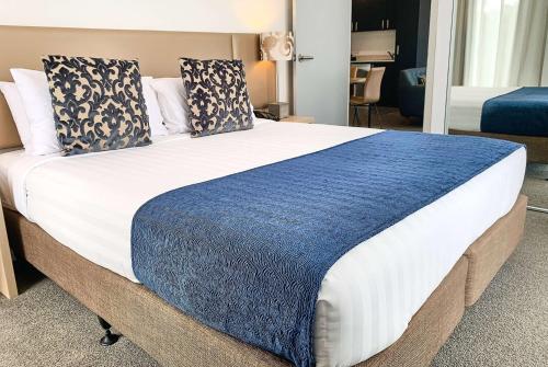 a large bed with a blue blanket on it at Ramada Suites by Wyndham Albany in Auckland