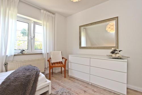 a white bedroom with a dresser and a mirror at Ferienhaus Ostseerausch in Scharbeutz