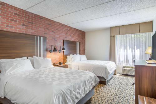 a hotel room with two beds and a brick wall at Burrstone Inn, an Ascend Collection Hotel in Utica