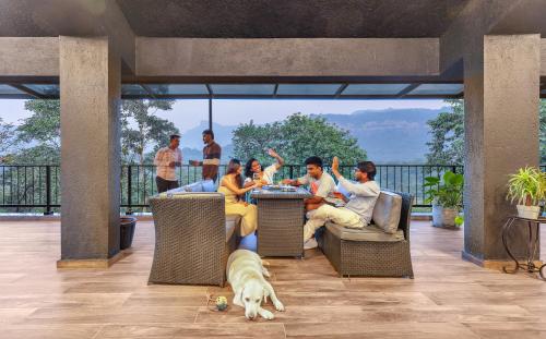 a group of people sitting at a table on a patio with a dog at SaffronStays Earl Grey in Khandala
