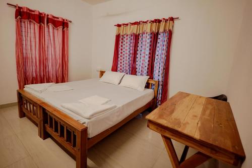 a bedroom with a bed and a table and curtains at Sherin Cottage in Varkala