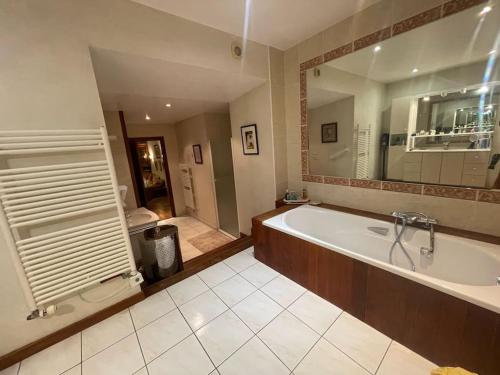 une grande salle de bain avec une baignoire et un grand miroir dans l'établissement Maison de famille entre lacs et montagnes, à Cusy