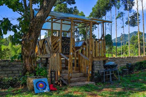a wooden house with a grill and a tree at Kitanda Msituni in Meru