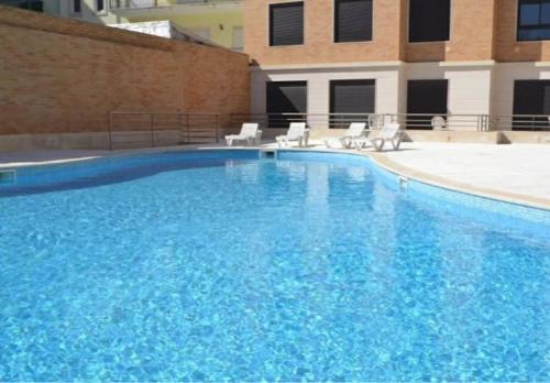 a large blue swimming pool with chairs and a building at Apartment T1 60 sq m for rent next to the bay in São Martinho do Porto