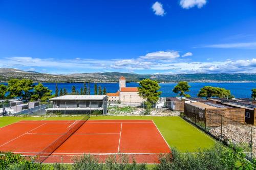 a tennis court with a house and the water at Apartments Villa Niko in Trogir