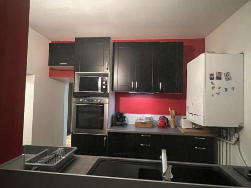 a kitchen with black cabinets and a red wall at La Lone 1870 in La Roche-de-Glun