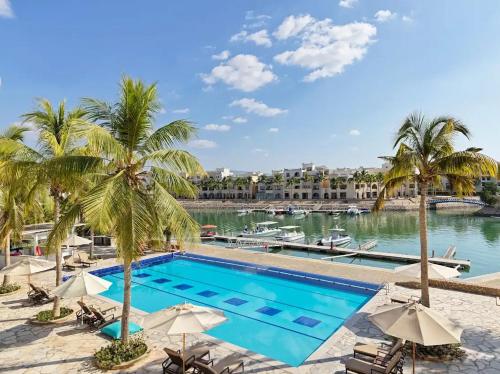 a pool with palm trees and a body of water at Beachfront Apartment with Pool & Stunning View in Salalah