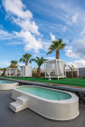 a resort swimming pool with a tent and palm trees at Smy Mediterranean White Santorini in Kamari