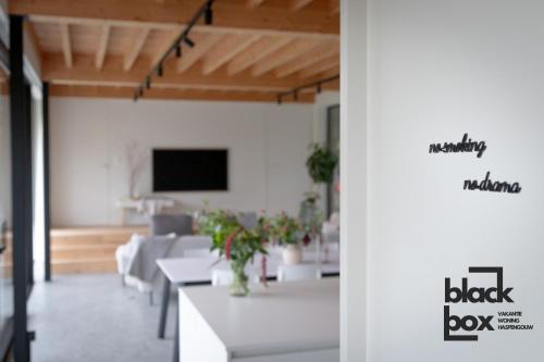 a living room with white tables and a flat screen tv at Black Box by De Schrijfbar - vakantiewoning Haspengouw in Wellen