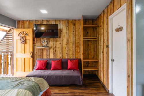 una camera da letto con pareti in legno e un letto con cuscini rossi di Pucón REC-Lodge Cabañas Las Bandurrias a Pucón