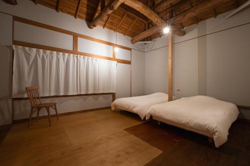 two beds in a room with a chair and a window at 港に停泊する町のフロント moyai 舫 in Choshi