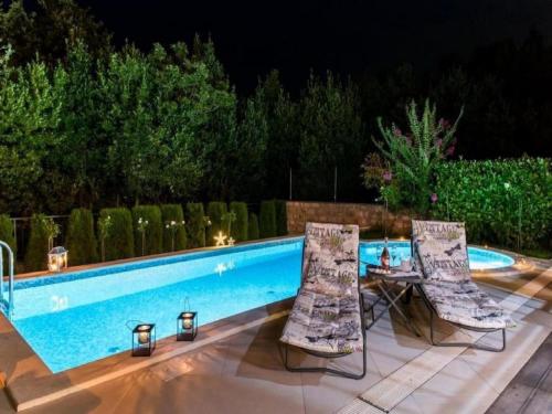 two chairs and a table next to a swimming pool at night at Beautiful Villa surrounded by Greenery with Swimming Pool in Gruda
