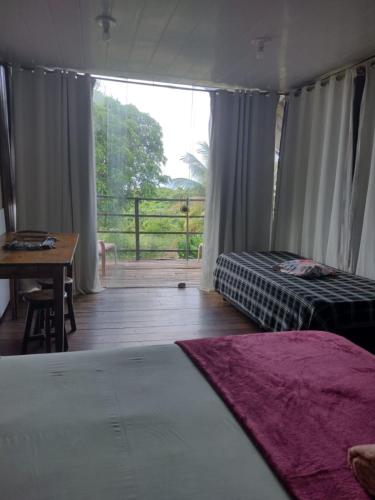 a bedroom with a bed and a table and a balcony at Palhoça da Colina in Fernando de Noronha